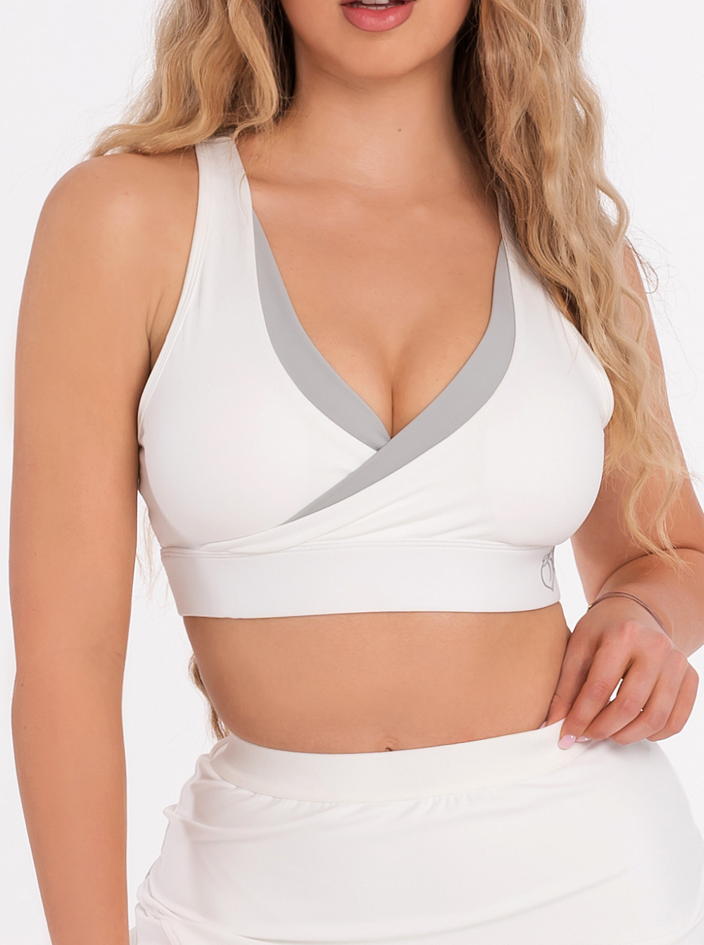 Biustonosz sportowy w kolorze białym z szarą lamówką i wkładkami, którą można wyjąć.